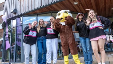 Student posing for a photo outside of claudia parsons with their hall mascot