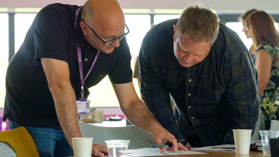 Two members of staff leaning over a desk in discussion