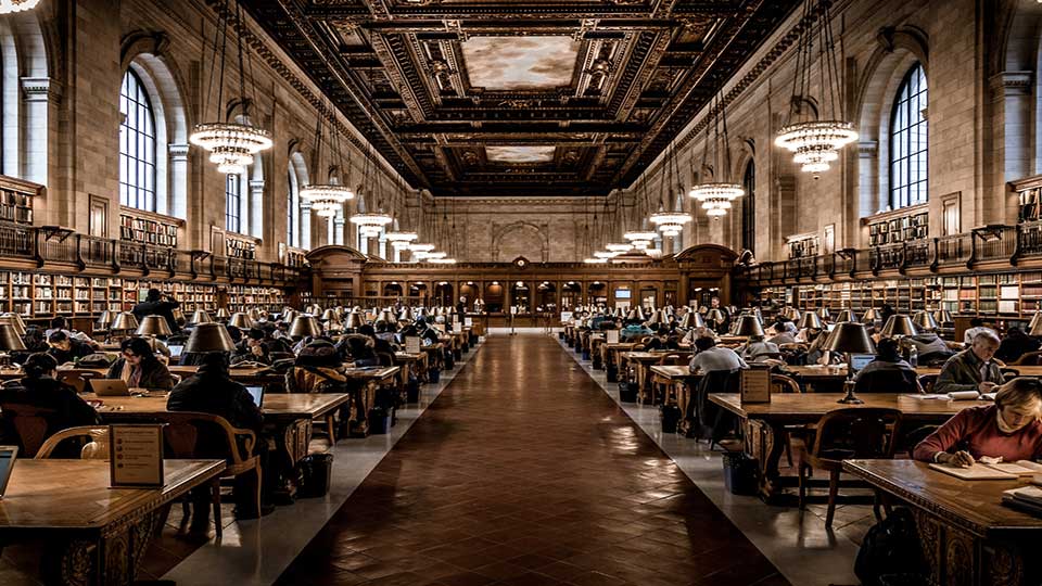 A shot of a library with high ceiling and people sitting at tables and reading