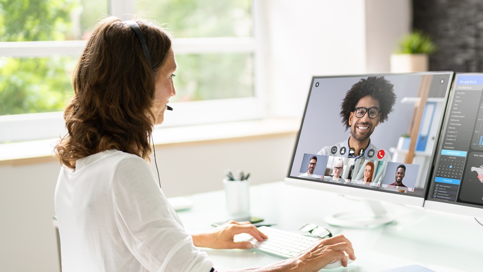 A person sat at a desk facing a computer screen. The screen shows other people in an online meeting or training session.