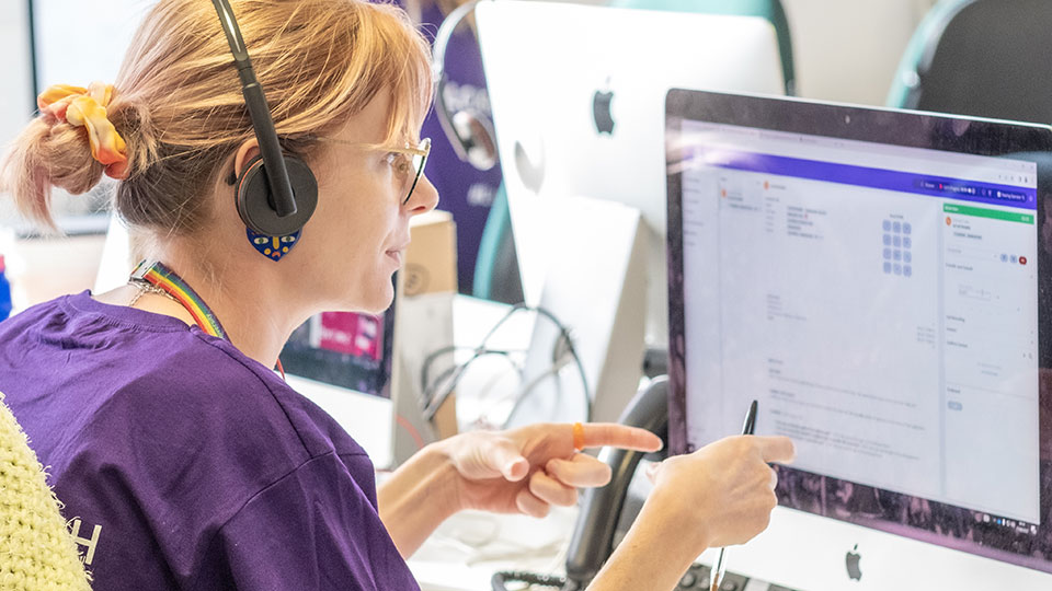 A call handler talking to a student on the phone using a telephone headset on results day, while looking at a computer screen