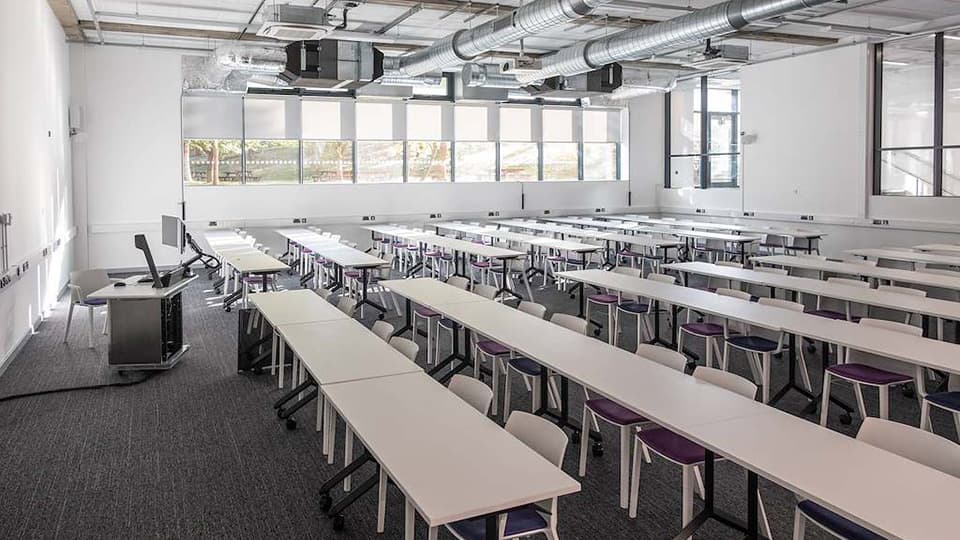 DAV019 - flat teaching space with grey carpet and white everything else - movable desks and chairs, with natural light mostly from side.