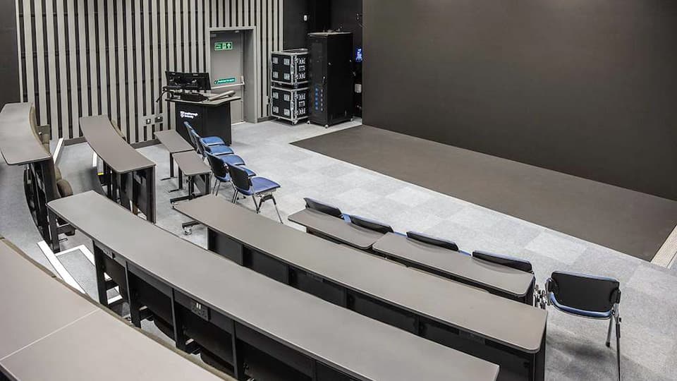 DigiLabs Central - DLC003 - Visualisation Theatre with tiered dark seating and desks, and black wall behind lectern..