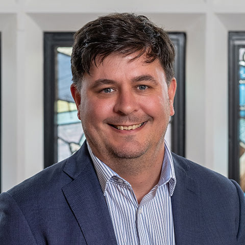 A portrait photograph of Dan Parsons against a stained glass background