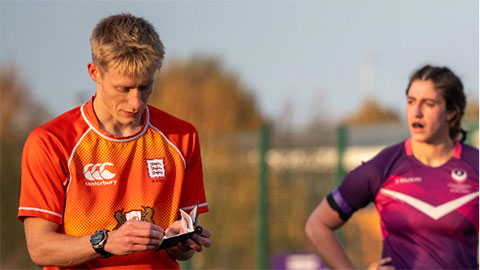 Will, on a pitch, writing in an officials notebook