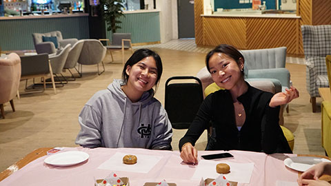 Two students sat at a table, looking at the camera smiling whilst attending the girls night in event