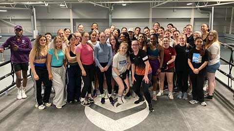 A large group standing together looking at the camera smiling, inside a boxing ring