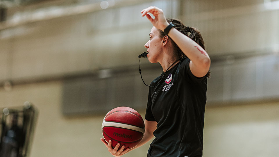 A match official blowing a whistle holding a basketball.