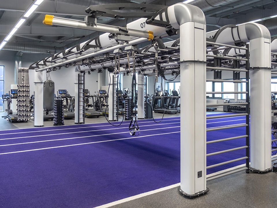 Large gym area with purple indoor running track, modular training rig, suspension straps, and various fitness equipment in the background.