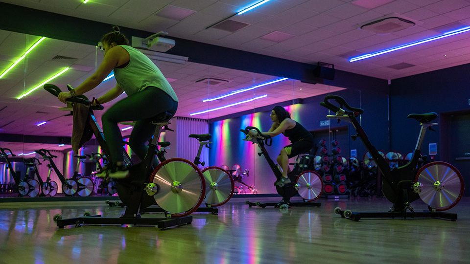 A fitness studio is lit up for a fitness class, with mirrors on all walls.