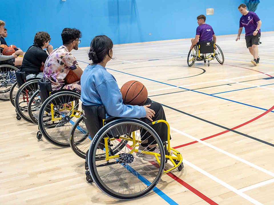 Students are playing Wheelchair Basketball in a sports hall.