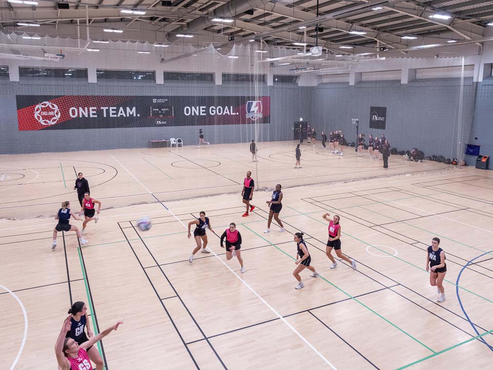 Groups of people are using the hall for different activities. It is split into 2 zones by a net down the middle.