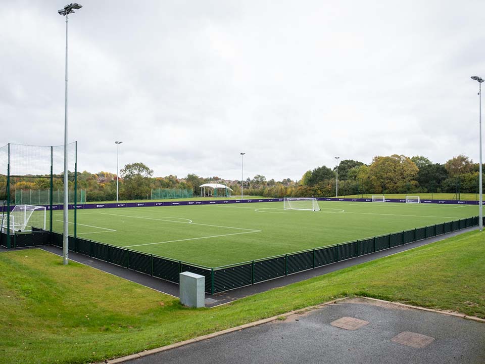 An artificial pitch with a purple boarding around it.