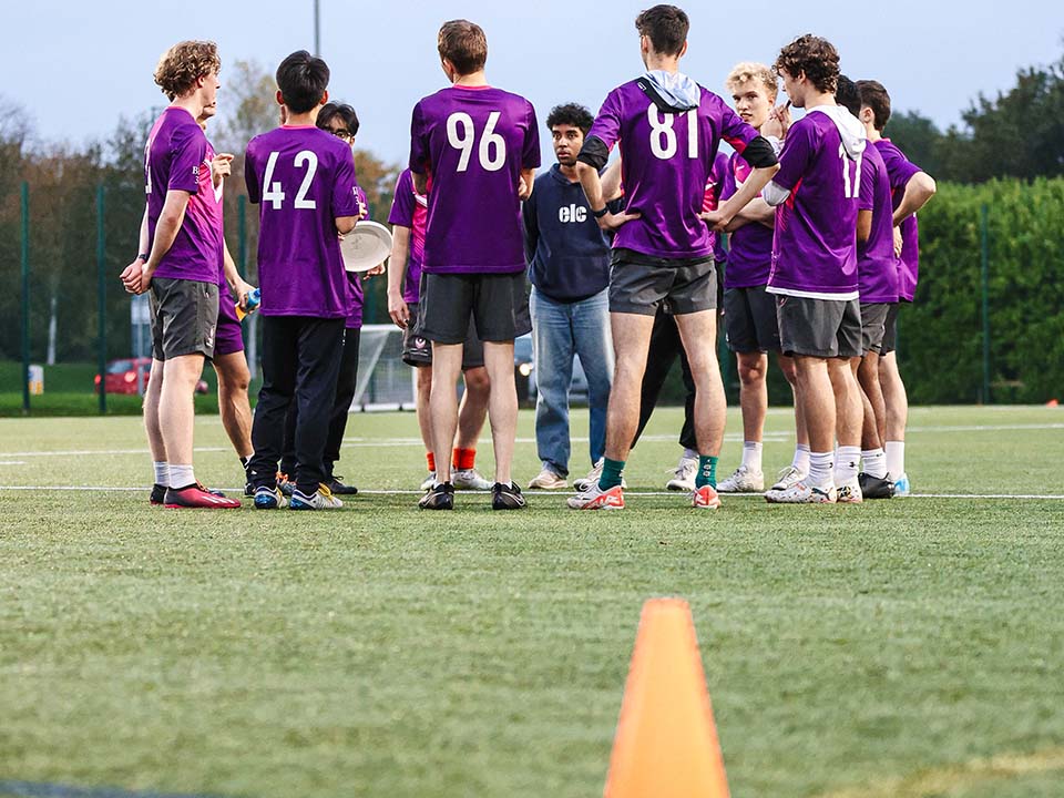 A team stand on the artificial surface in a huddle.