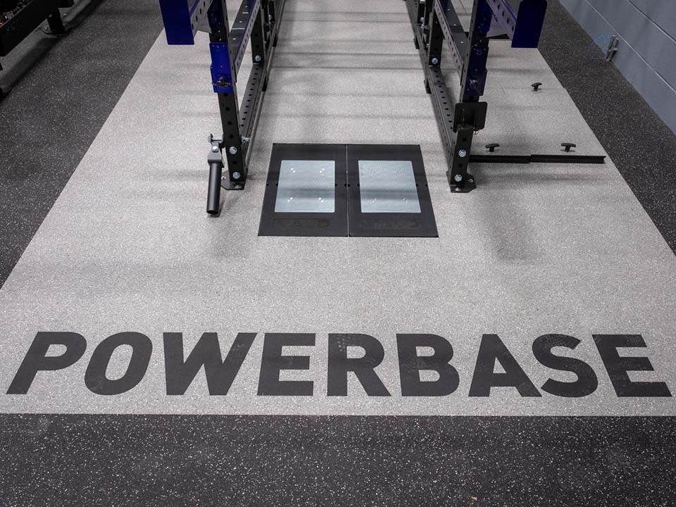 A pair of force plates sit in the floor under a squat rack.