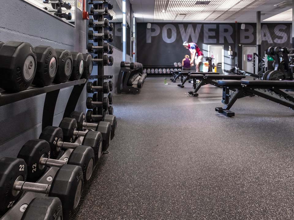 Along a wall, there are dumb bells lined up infront of workout benches.