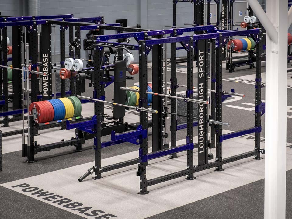 Powerbase has purple squat racks with accessible weights next to them, with 2 bars each and a smith machine in the middle.