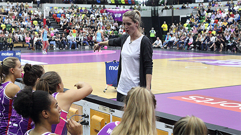 a woman talking to players at the side of the court