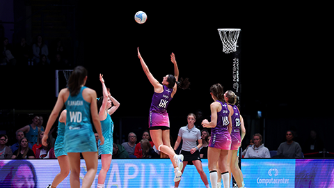 Netballer shooting at the post with defender jumping to attempt a block