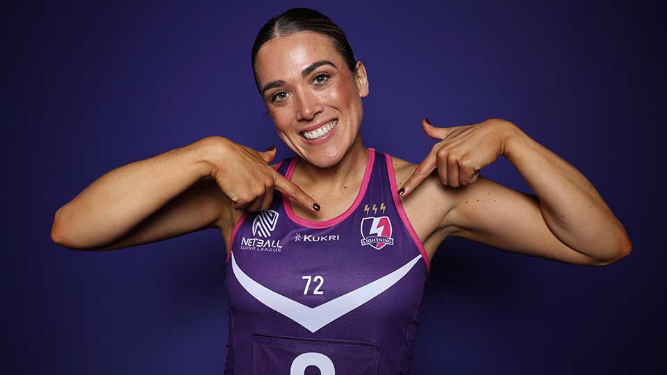 Headshot of Nat, smiling, pointing at the Loughborough Lightning badge on a jersey