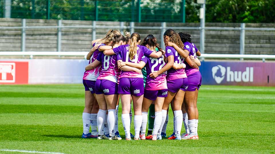 Loughborough Lightning Football team standing in a team huddle on a football pitch