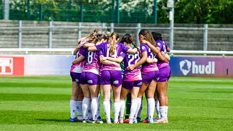 Loughborough Lightning Football team standing in a team huddle on a football pitch