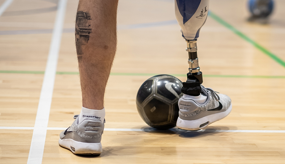 close up of a person's legs and a football, one leg is prosthetic.