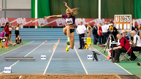 female triple jumper in mid-air above sand pit
