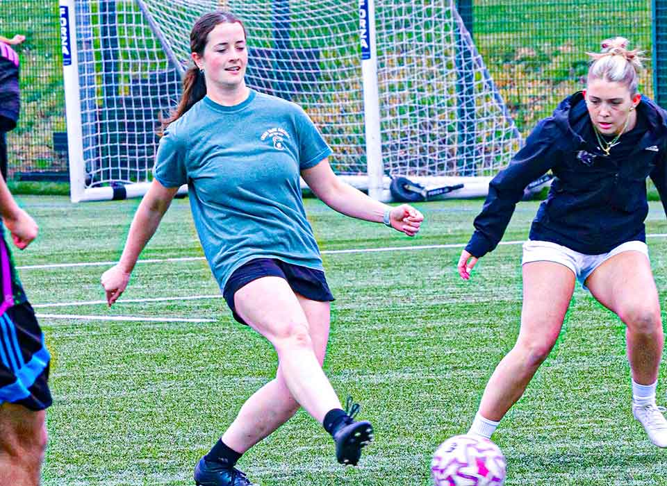 student kicking a ball on a football pitch