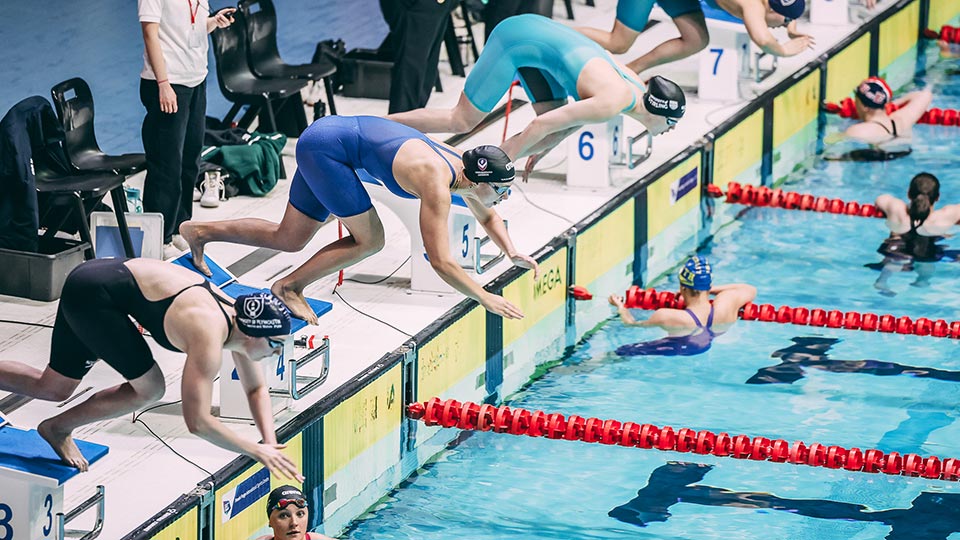 A swimming relay with swimmers in the pool and swimmers about to jump in.