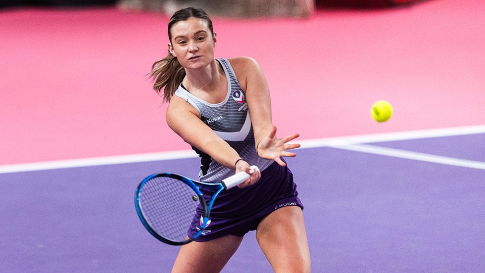 A female tennis player on the court holding a racket and about to hit the ball