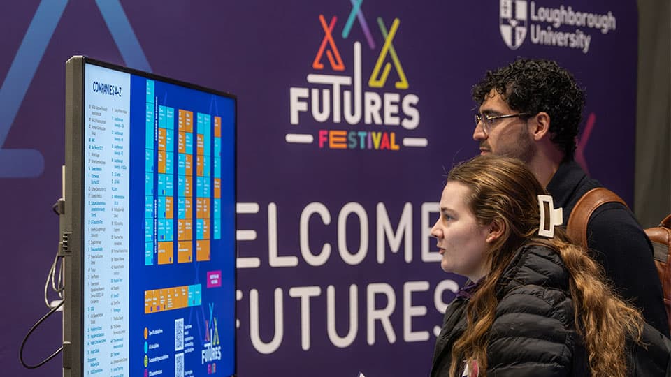 Two students look at the fair floorplan, standing in front of a purple fair banner.
