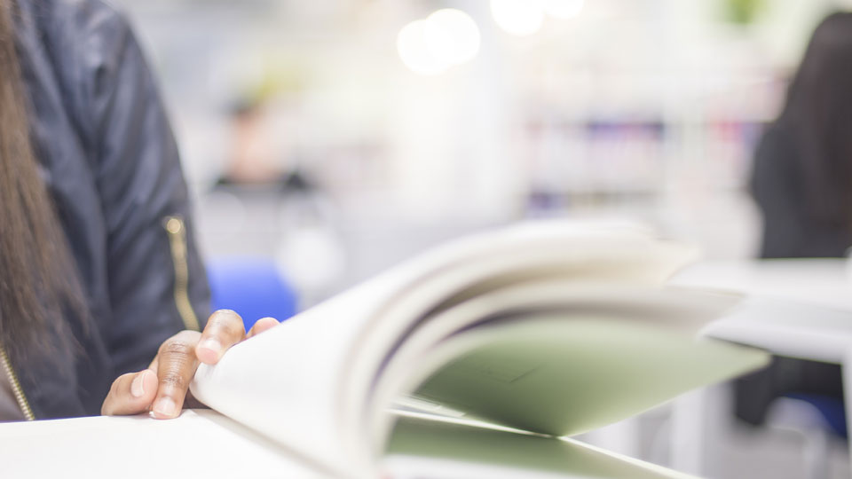 a close up of a woman reading a book with a figure in the distance behind
