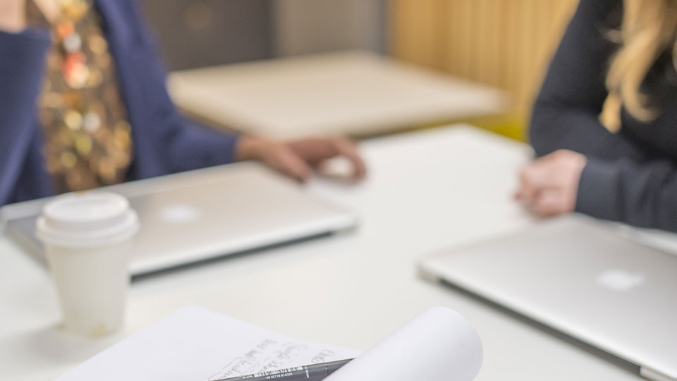 two people sitting at a table, laptop and book on the table