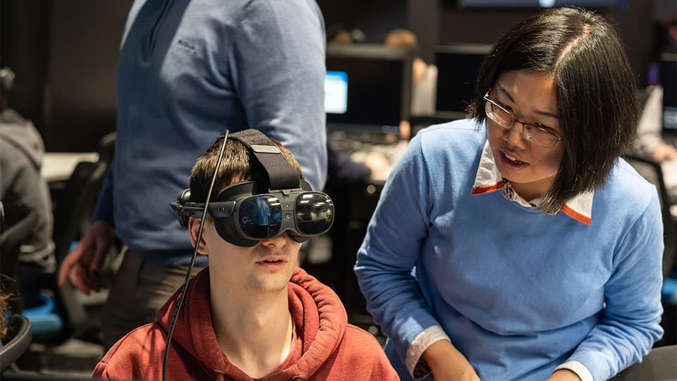 A student wearing specialiased googles and interacting with an instructor in a VR lab session.