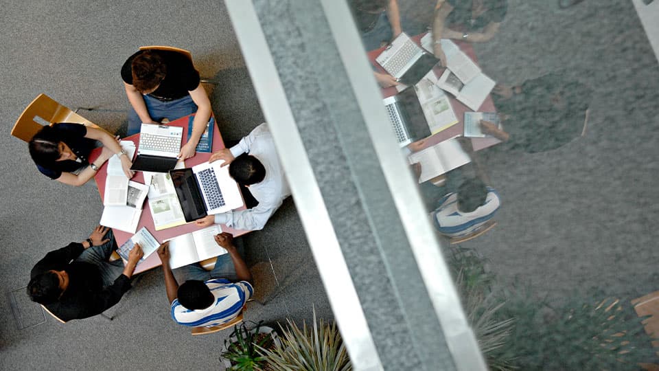 five people having a meeting around a table with their laptops in front, a photo taken from above