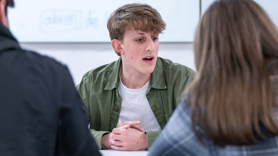 A male student talking to two other students (their backs are to the camera)