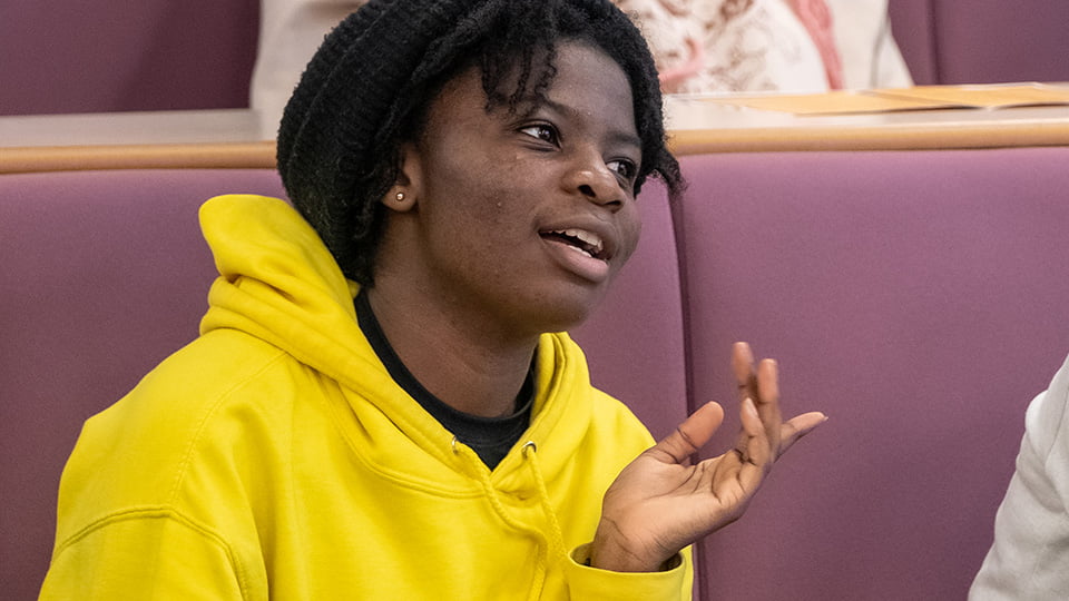 A student in a bright yellow hoodie sitting talking in a lecture theatre