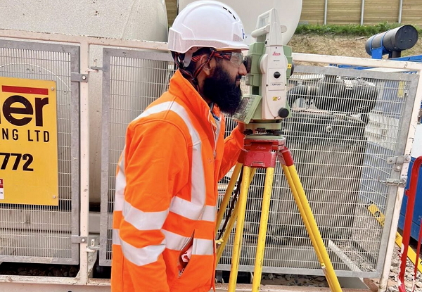 Image of Tayeb on site at Balfour Beatty wearing an orange hi-viz and using some measuring equipment 