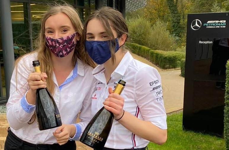 Image of Rebecca and a colleague holding a bottle of wine outside her Mercedes office.  