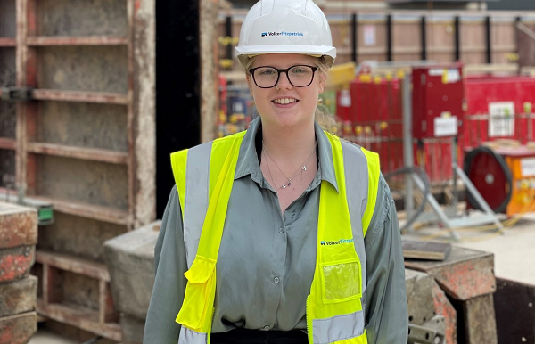 Image of Danielle on a building site with an yellow hi-viz and a white hard hat. 