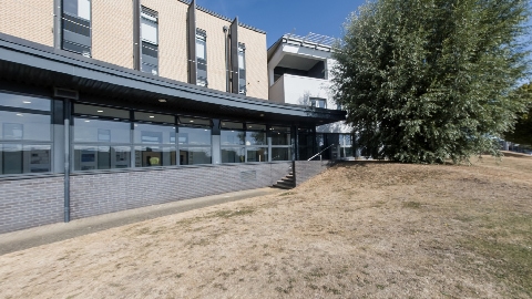 Exterior view of a modern academic building with large windows, landscaped grounds, and a tree-lined courtyard.