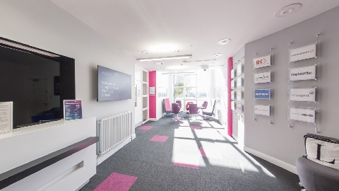 Reception and waiting area with lounge seating, meeting space, and display boards featuring company and partner logos.