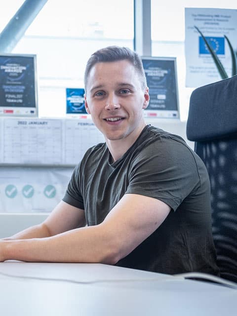A person sitting at a computer desk smiling towards camera.