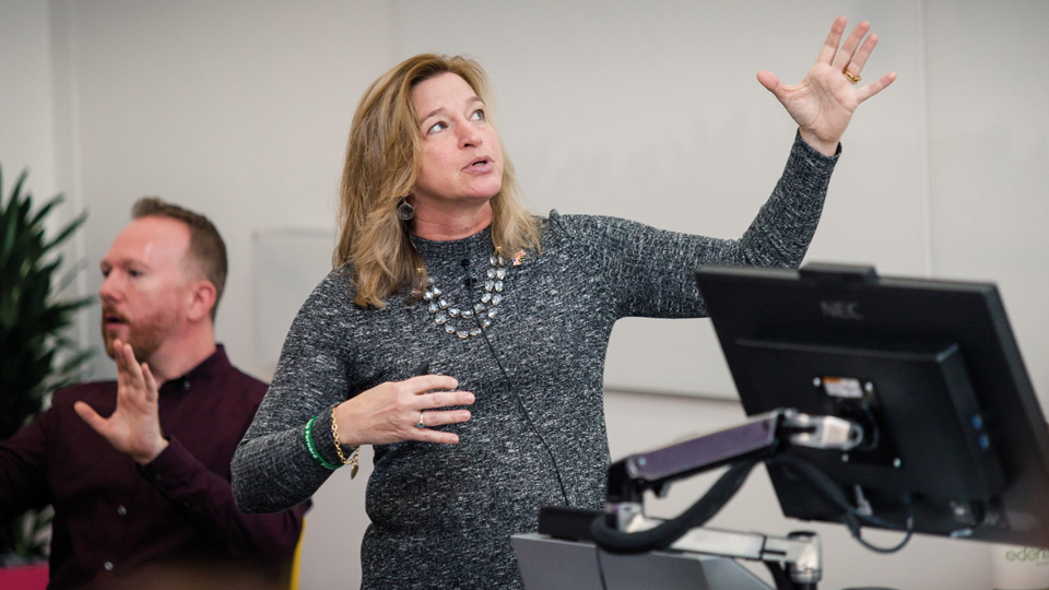 a lecturer gesturing towards a presentation