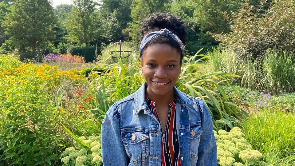 Student stood outside in a garden with lots of plants in the background.