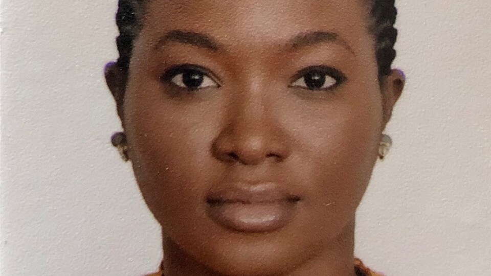 Female student smiling at the camera in front of a white background, wearing gold earrings.