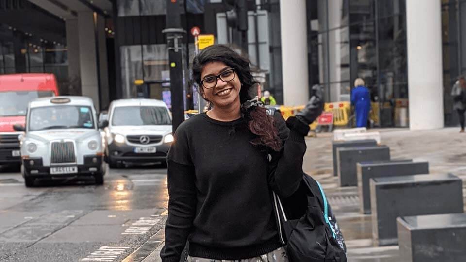 Student standing on a street smiling with busy London traffic in the background
