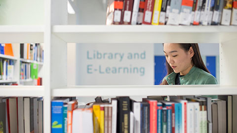 A student standing behind a shelf with books on at Loughborough University London