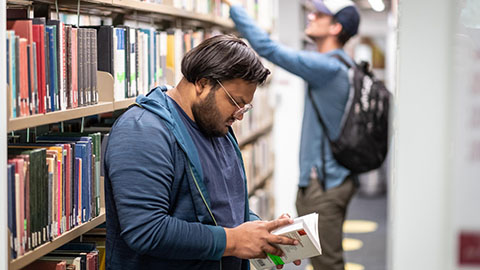 Two students looking at books in the University library